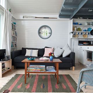 living room with porthole windows painted panelling bookshelves and white curtains billowing in the breeze