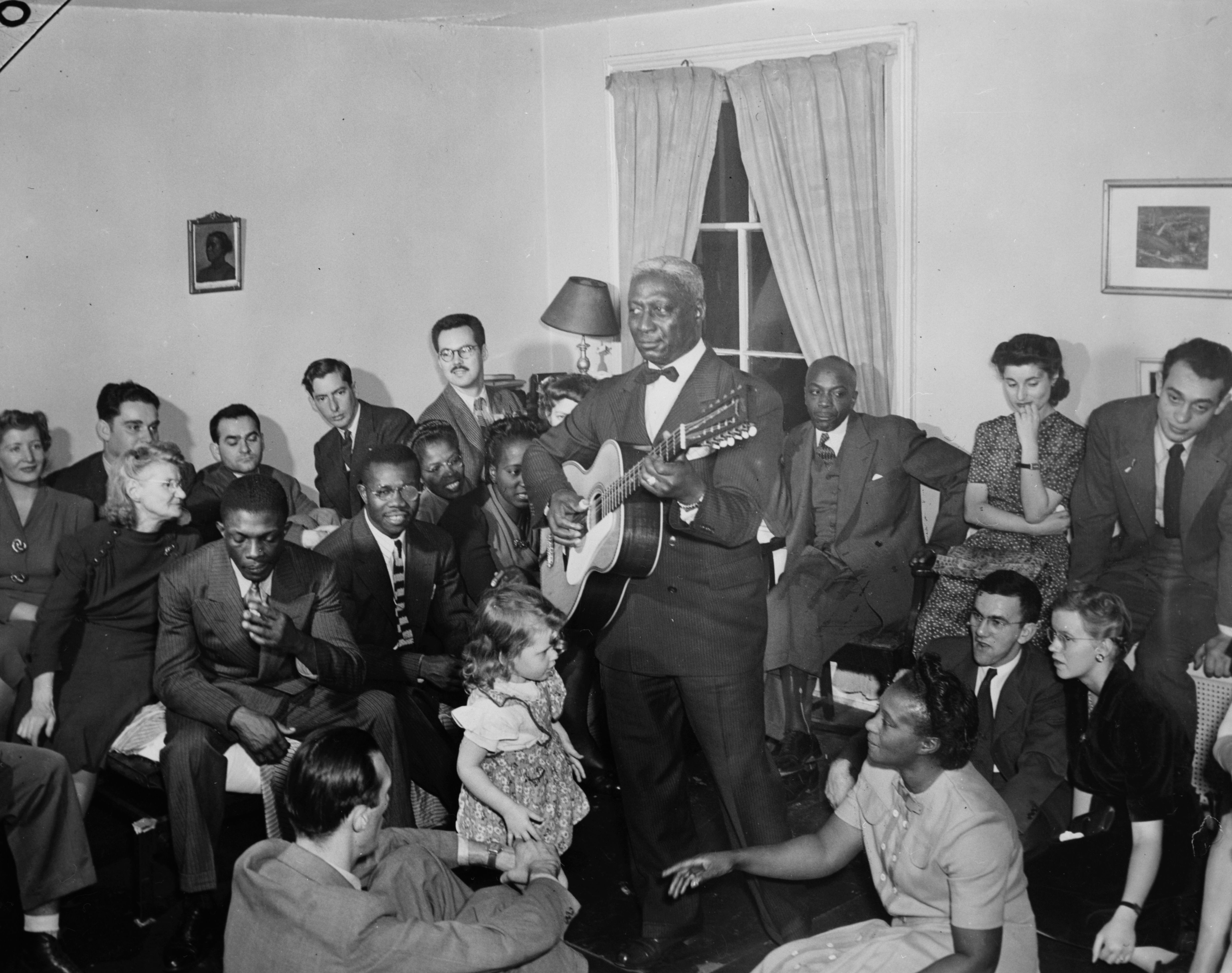 Huddie Ledbetter, better known as Leadbelly, sings and plays the guitar for a room full of people