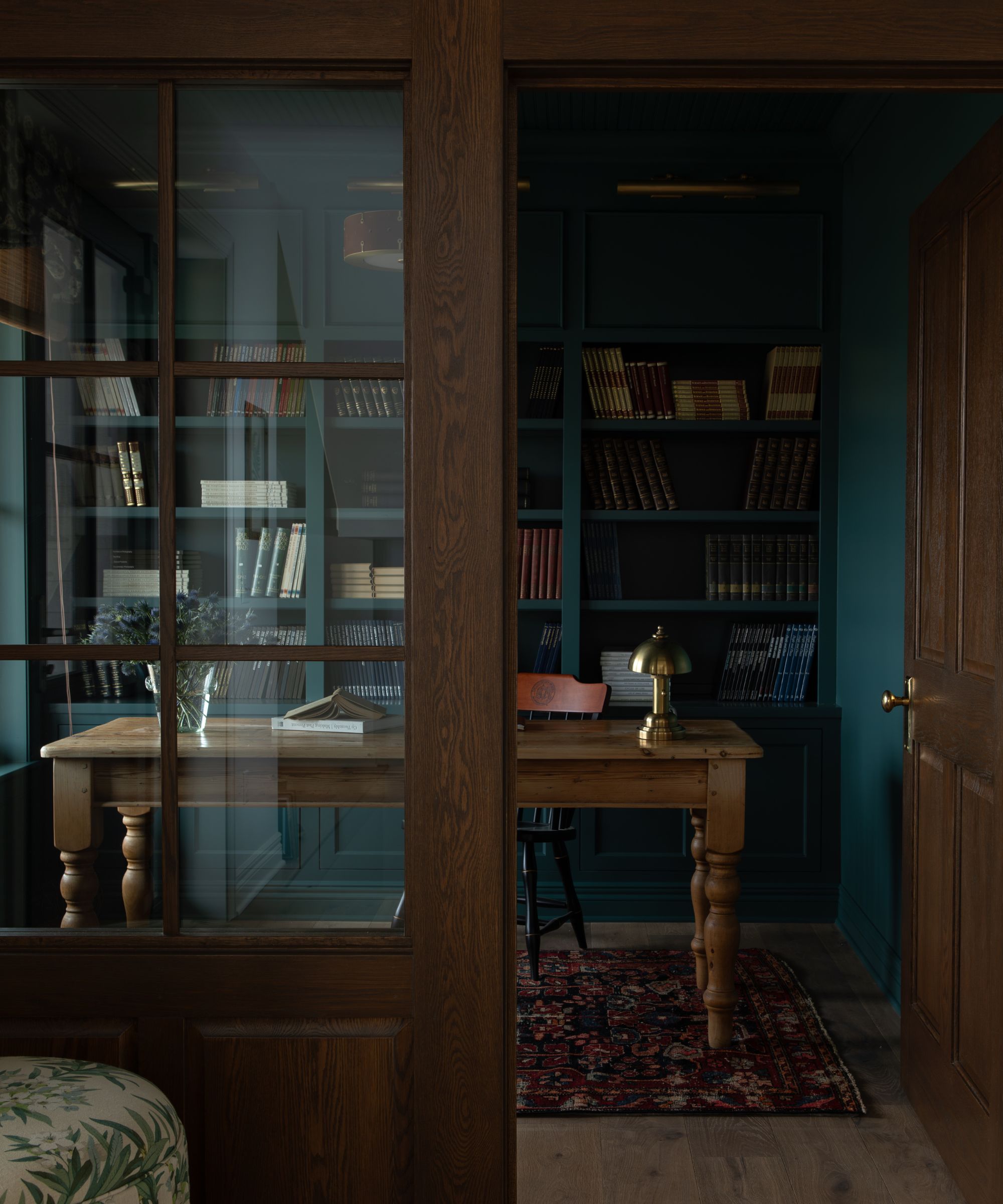 A study room color-drenched teal with a vintage desk, built-ins, and wooden and glass doors.