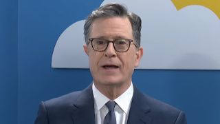 Stephen Colbert standing in front of a back drop with clouds and a sun in The Late Show with Stephen Colbert