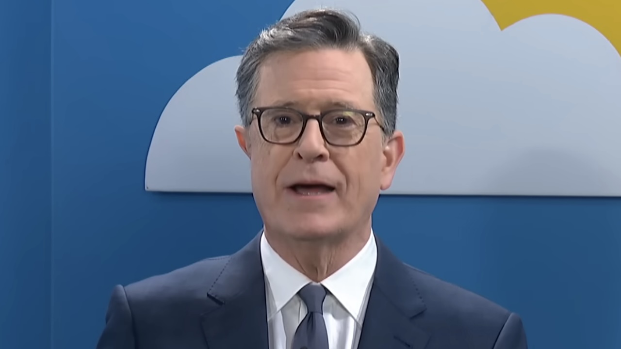Stephen Colbert standing in front of a back drop with clouds and a sun in The Late Show with Stephen Colbert