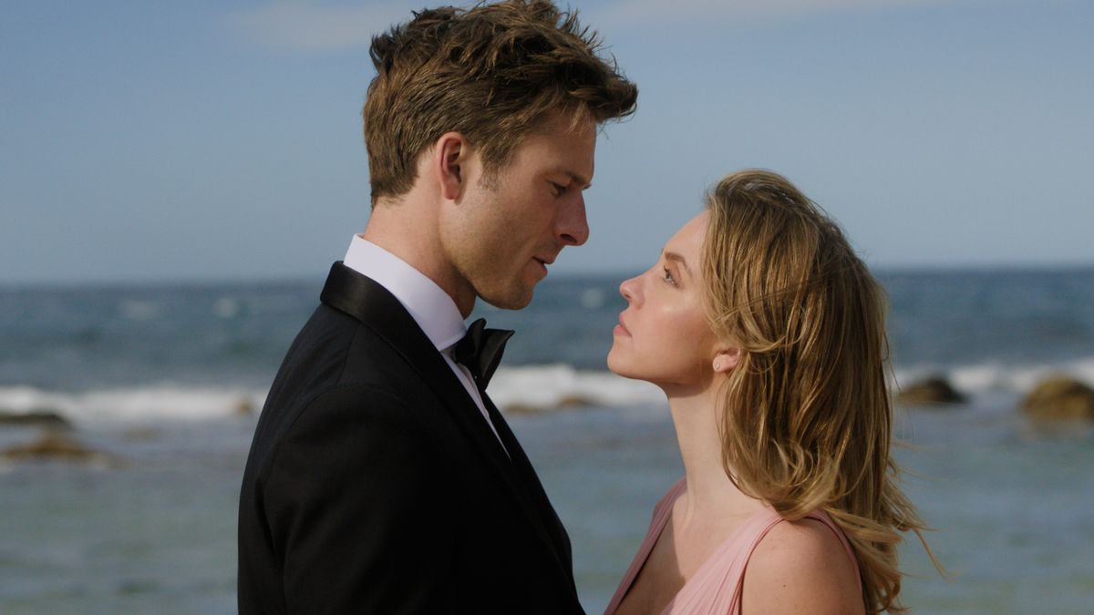 Glen Powell and Sydney Sweeney in formal wear looking into one another&#039;s eyes on the beach in Anyone But You