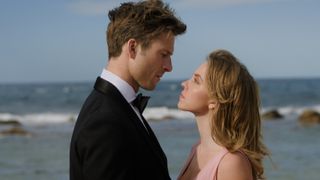Glen Powell and Sydney Sweeney in formal wear looking into one another's eyes on the beach in Anyone But You