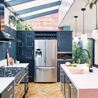 silver fridge freezer within blue cabinets with a skylight, kitchen island with pink worktops and wooden flooring