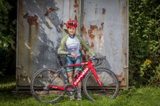 Jen George leaning on her bike in front of a large door with flaking paint