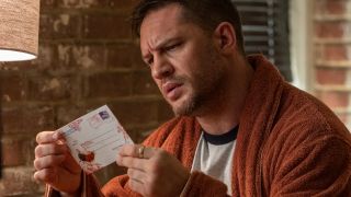 Tom Hardy examines a postcard in Venom Let There Be Carnage.