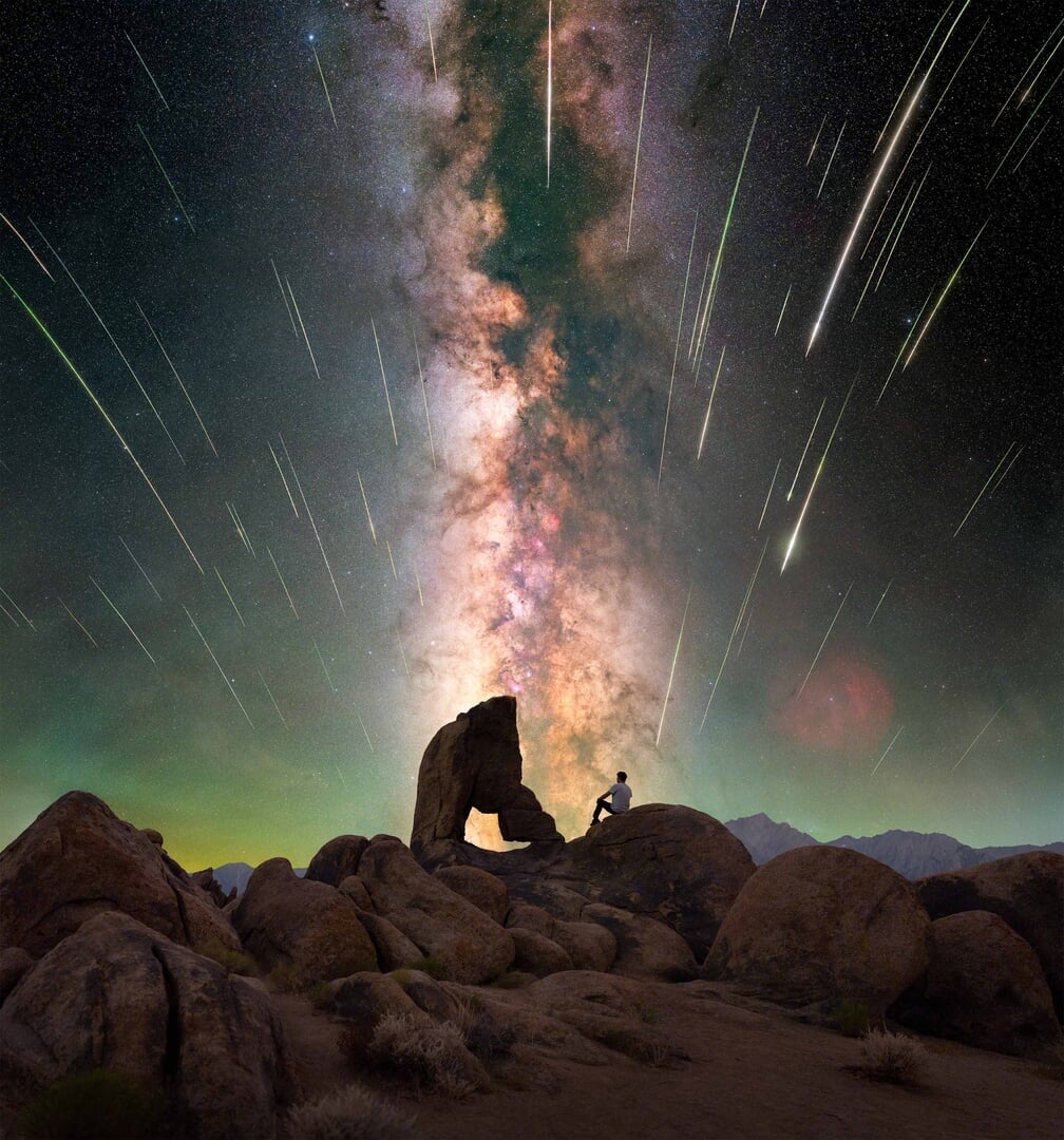 A photo of shooting stars in the sky with the Milky Way visible in a desert landscape