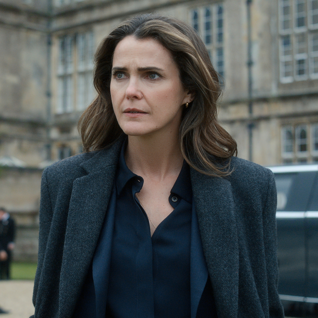 Keri Russell as Kate Wyler, standing in the driveway of a British castle, with suited men and black cars behind her, in 'The Diplomat' season 4.