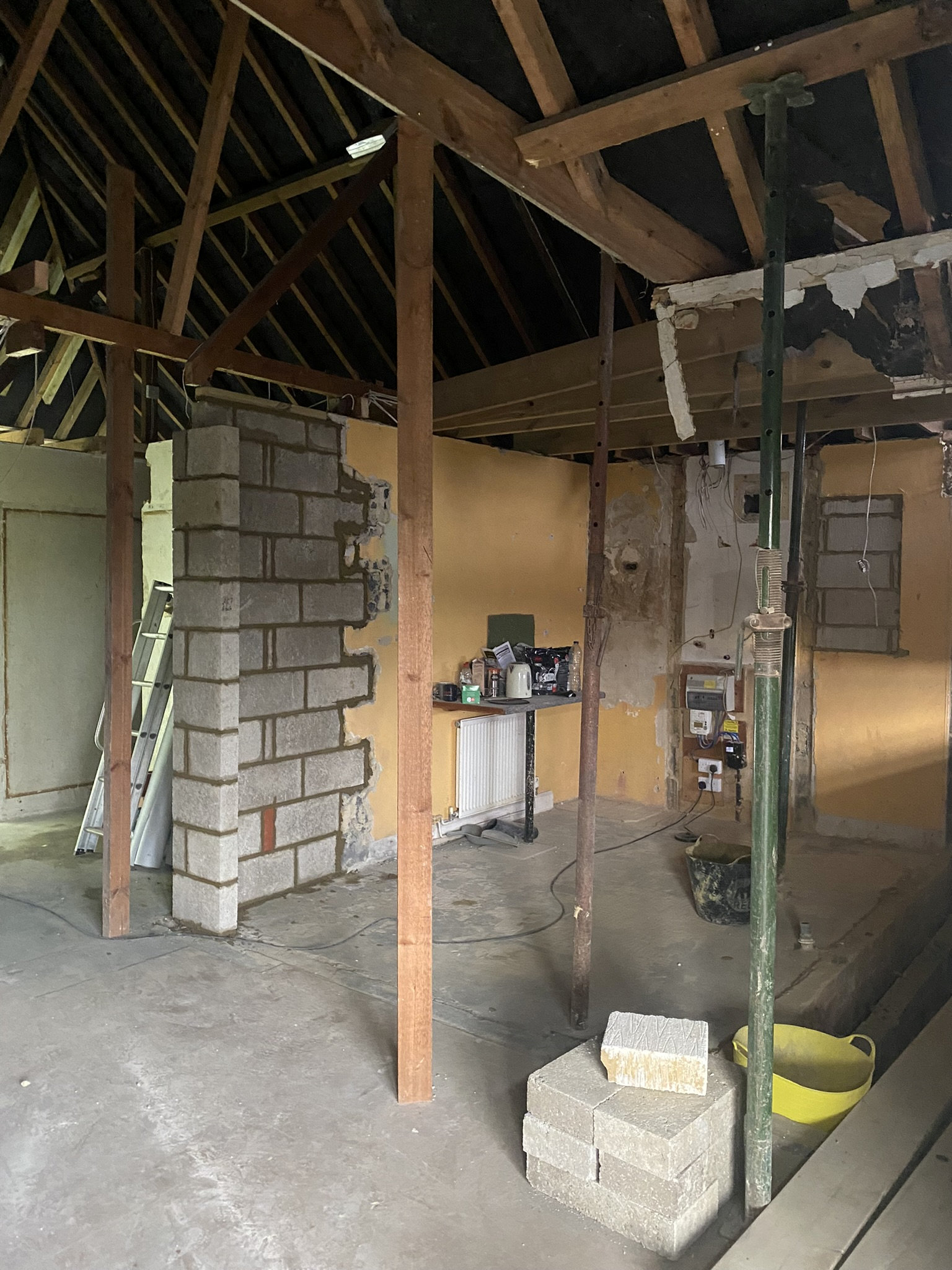 The bungalow during the renovation with a wall being knocked down and exposed brick and scaffolding poles holding up the structure