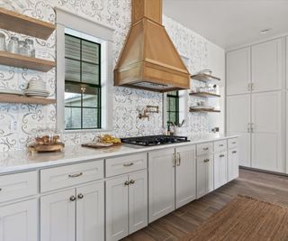 A kitchen with gray cabinets, a wooden range hood, and a patterned tile backsplash taken to the ceiling