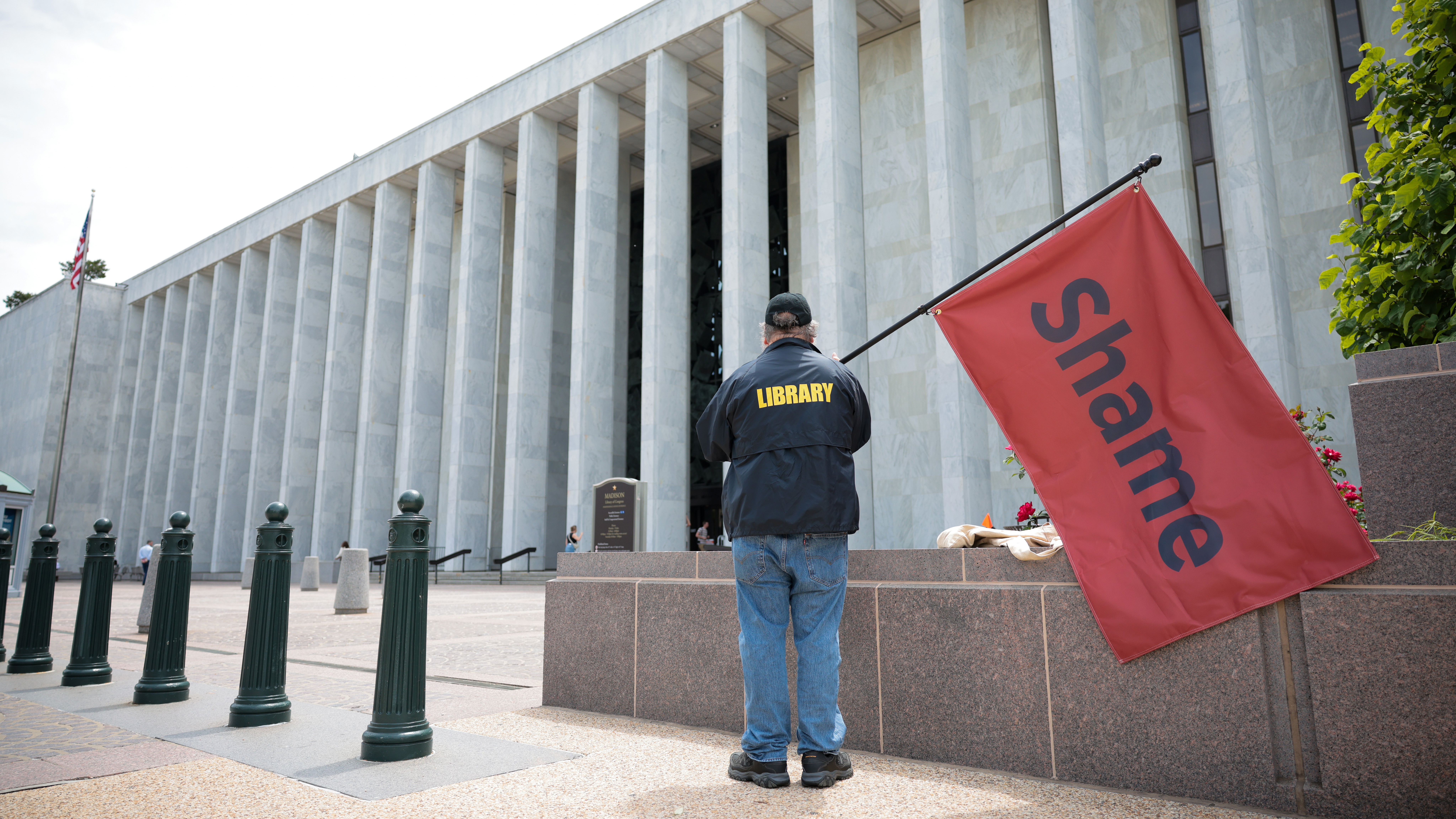 A man holds a red flag that reads "shame" outside of the Library of Congress