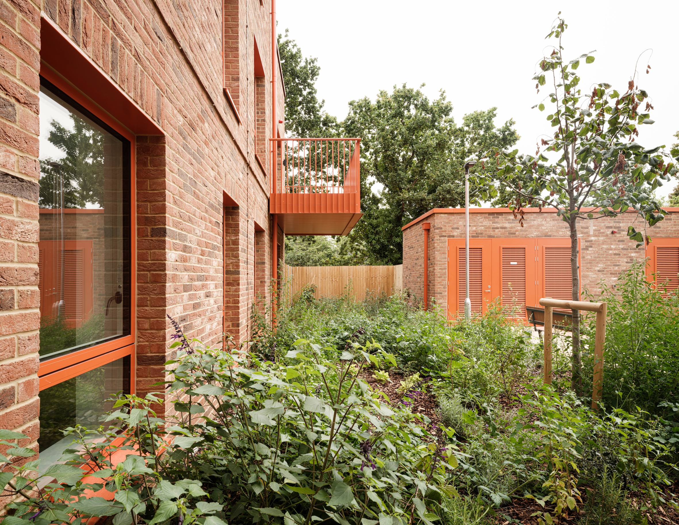 view of Farmstead Road, a brick residential complex in south london by metropolitan workshop. it features green gardens and orange metal details such as window frames and balconies