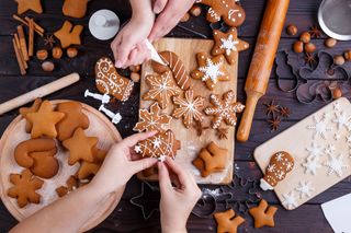 Two people decorating gingerbread Christmas cookies on a wooden table.