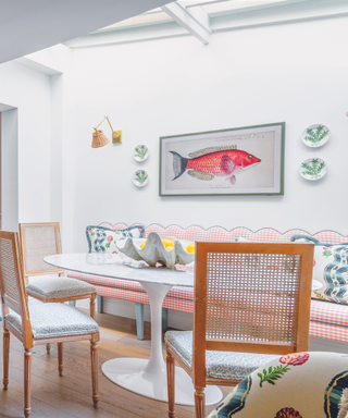 dining area in kitchen with inbuilt bench and gingham check fabric and rattan chairs around marble tulip table with fish art on wall and skylight