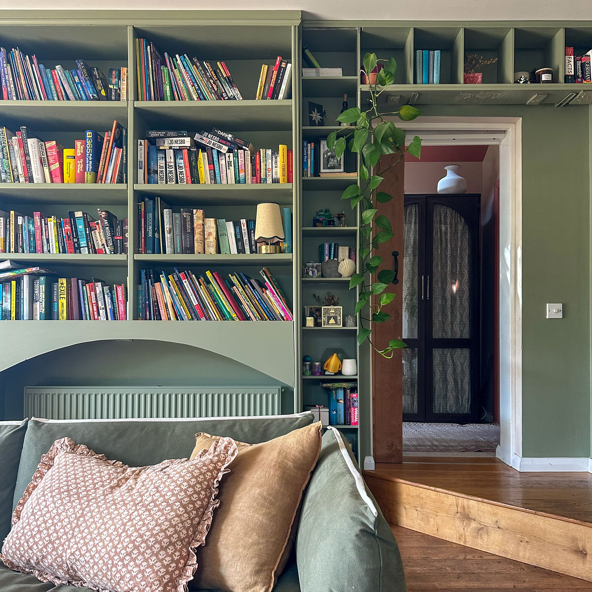 Living room with green bookshelves and colour drenched radiator underneath. Green sofa with neutral cushions