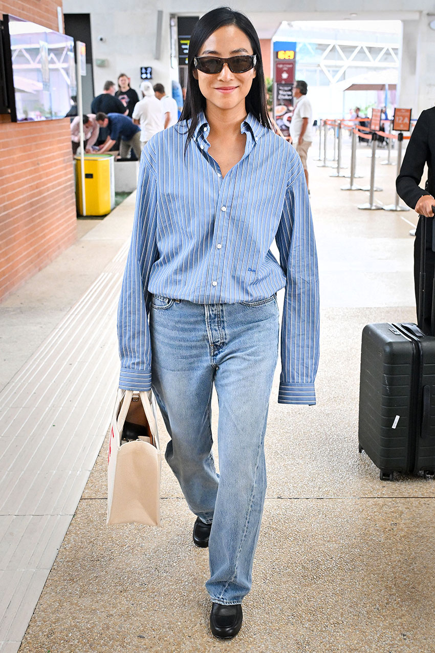 Greta Lee wearing a striped button-down shirt, blue jeans, and black boots