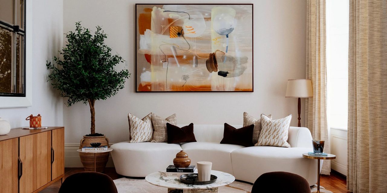 A lounge filled with earthy-toned design objects and furniture such as 1970s-style oversized sofas, coffee table collectibles, artwork, and plants, is filled with natural light.