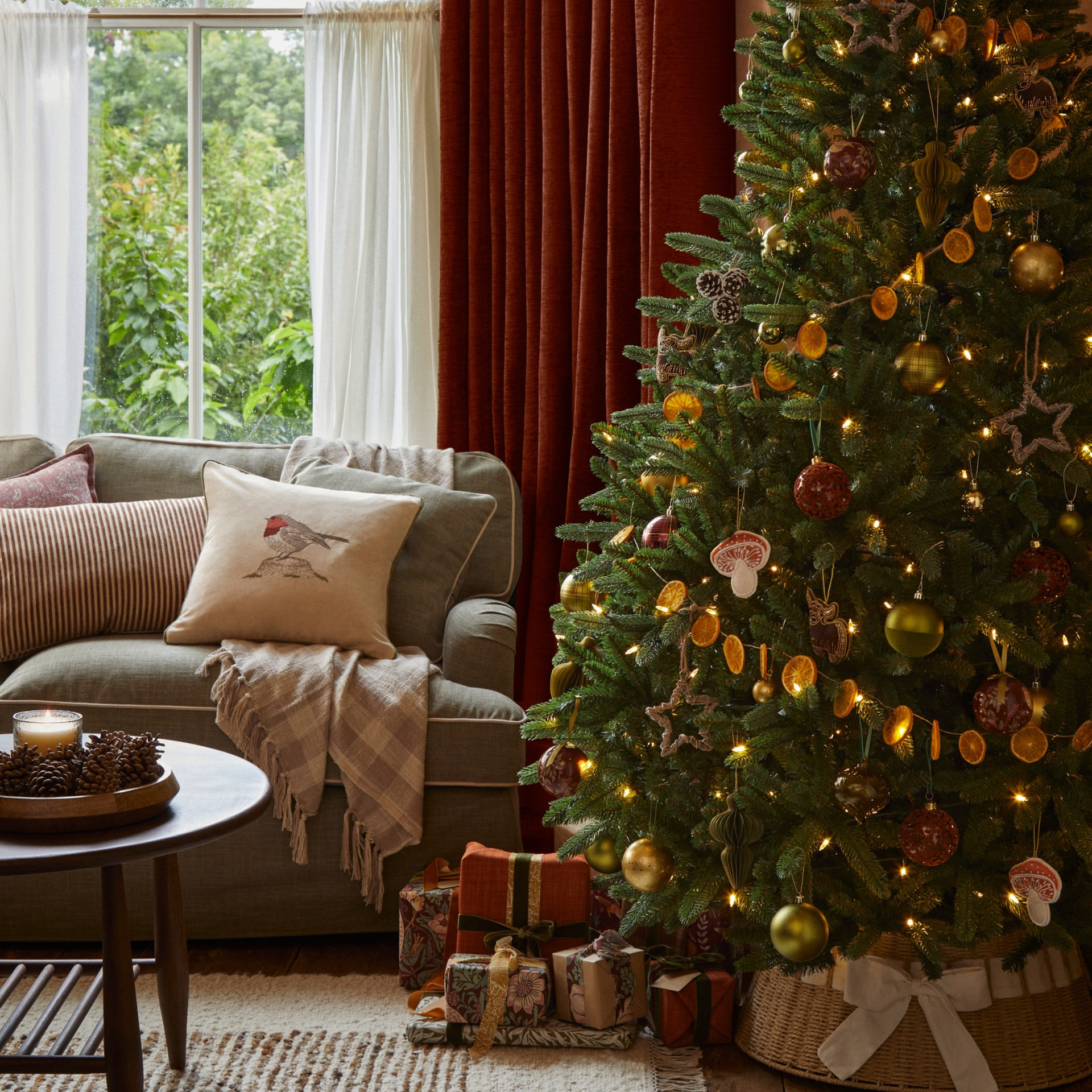 Sofa with robin cushion next to Chrismas tree with dried orange garland, orange baubles, mushroom baubles, stars and fairy lights.