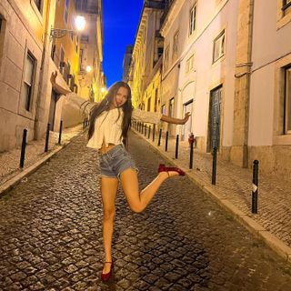 Olivia Rodrigo wears a white blouse with denim shorts and red Mary Jane shoes.