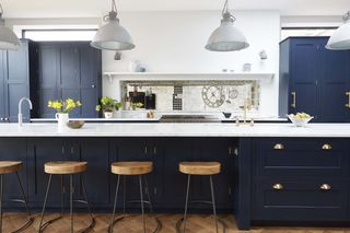 A blue kitchen with a large island with bar stools and clerestory windows above wall cabinets in the kitchen extension