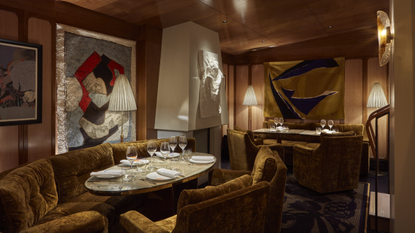 A golden-lit restaurant dining room draped in plush fabrics, velvety banquettes, and colorful artworks, as well as sculptures.