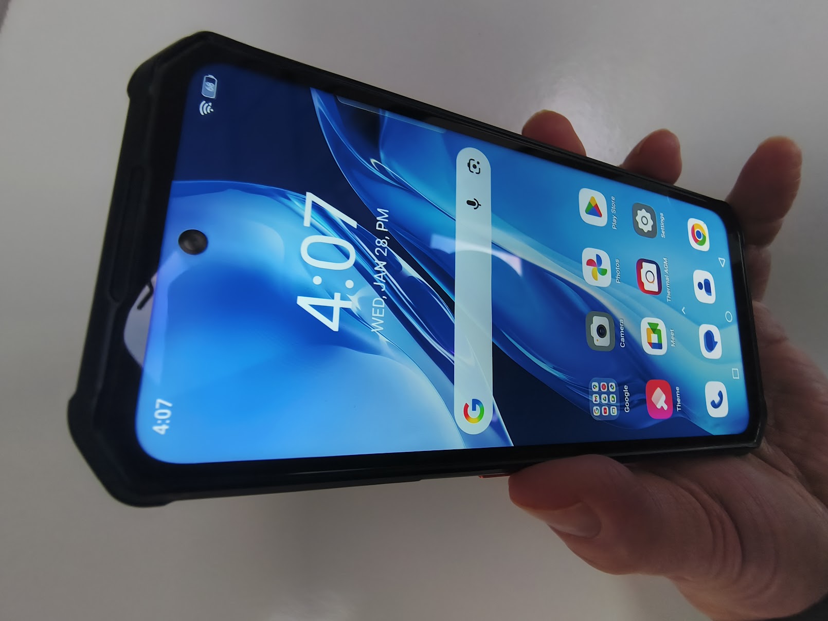 A hand holds the AGM G3 Pro at an angle, displaying the vibrant colors of the screen and the centered hole-punch front camera.