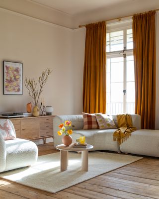 neutral living room with pops of orange, cream boule sectional, rug, retro sideboard, small coffee table