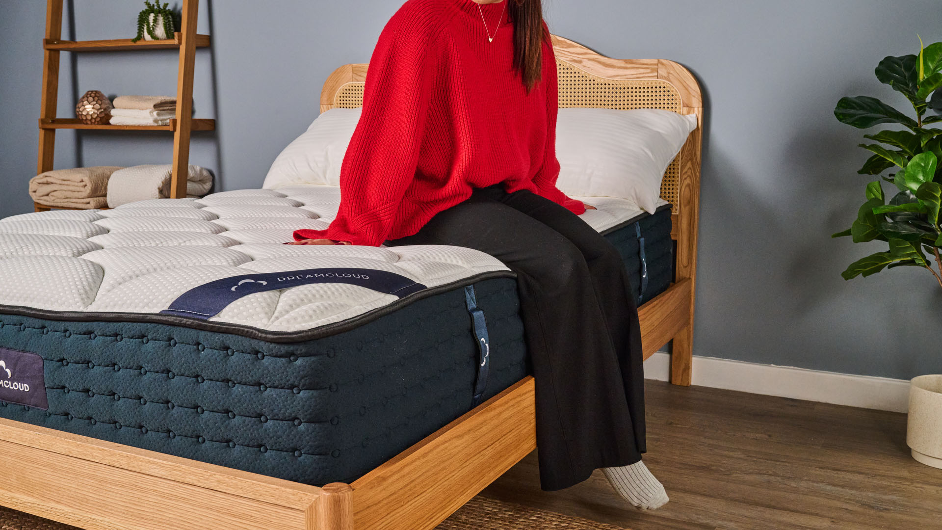 A woman sits on the side of the DreamCloud Hybrid mattress to test the edge support