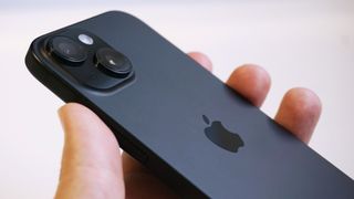 iPhone 15 i mörkgrått hålls upp med baksidan vänd uppåt.