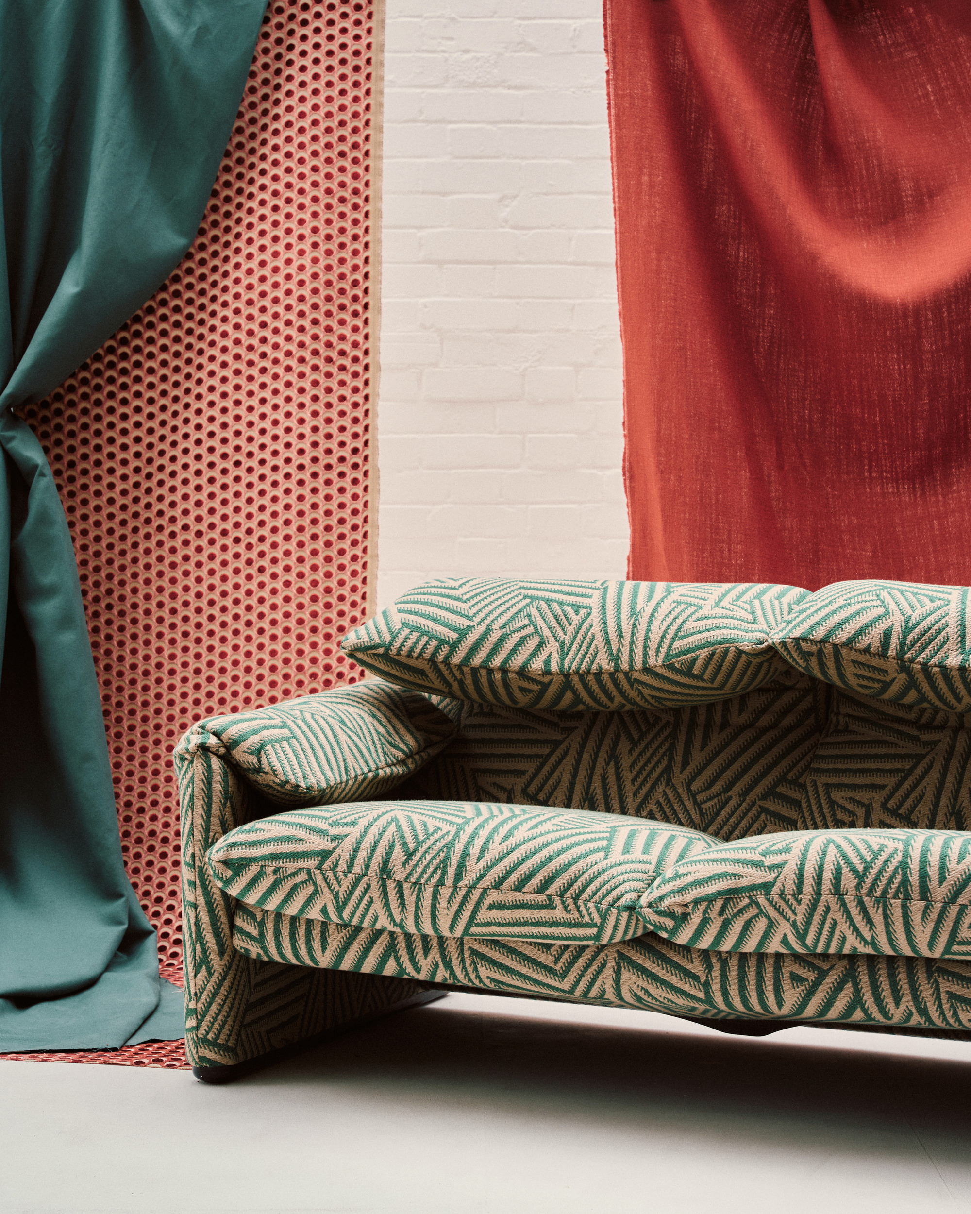 Image of an overstuffed modern sofa with a green and white print in a stage room with red and teal fabrics hanging from the ceiling.