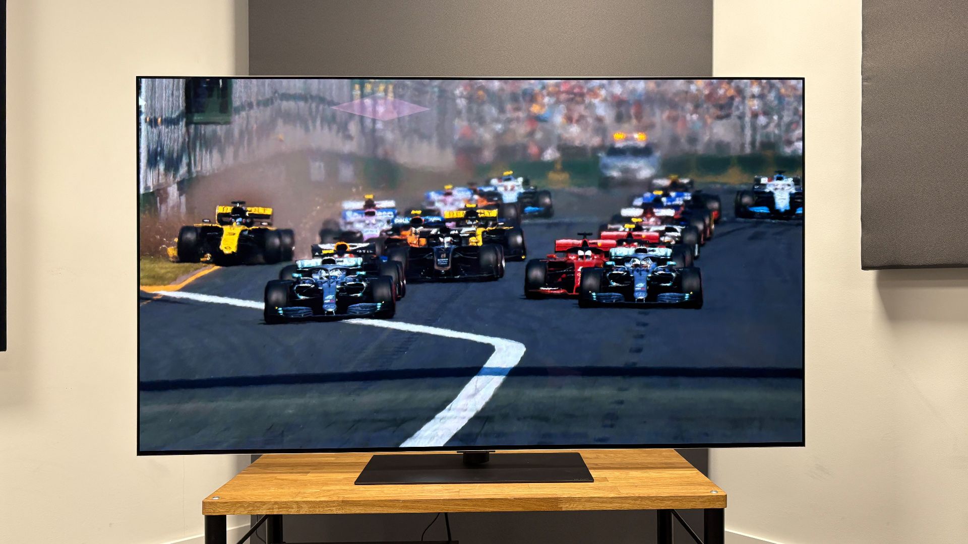 The 65-inch LG G5 OLED TV pictured on a wooden rack. On the screen is a still from Netflix F1 series Drive to Survive.