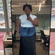 Chichi takes mirror selfie in white tshirt, black slip skirt, blue scarf around the waist, and silver shoes and jewelry