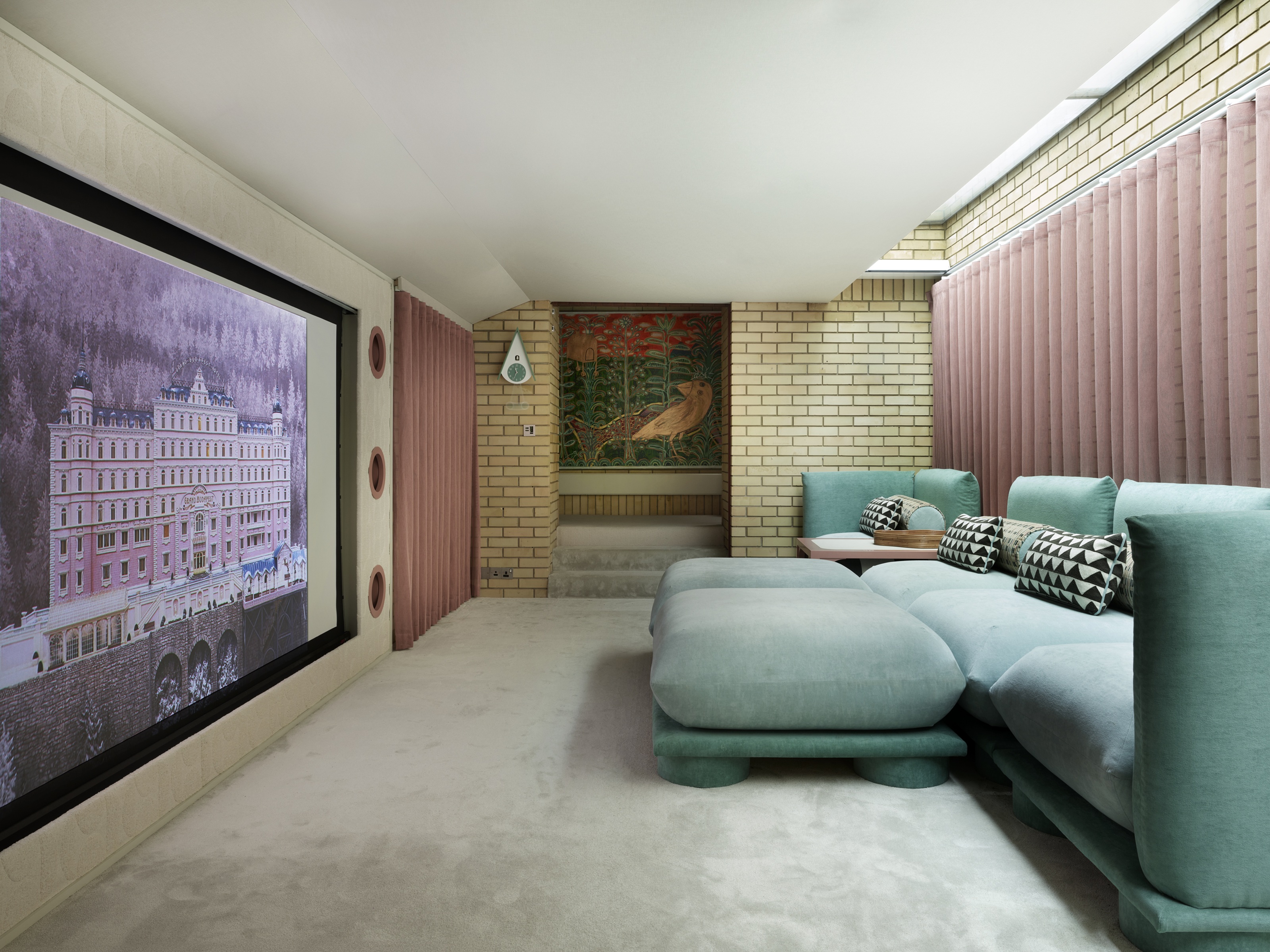 a home cinema with a pink curtain, teal sofa and large screen