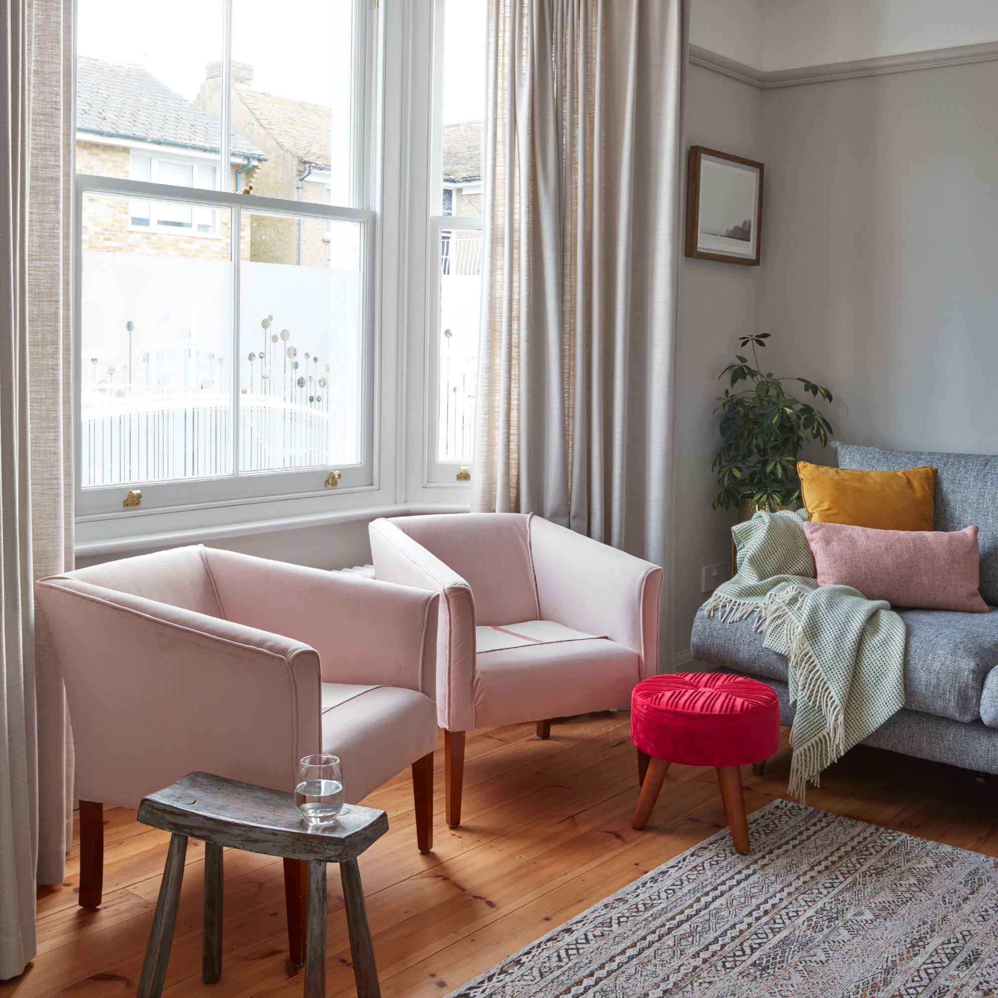 A grey living room with a grey sofa and two pale pink armchairs