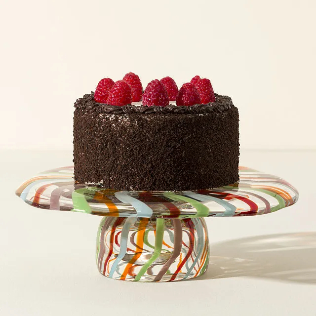 A colorful cake plate with a chocolate and raspberry cake on top of it