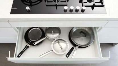 white kitchen drawer below a hob showing pot and pan storage ideas using a deep, pull-out drawer