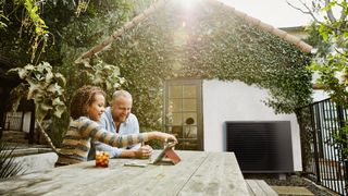 A heat pump in the sun against a brick wall whilst a happy couple sit outside alongside it