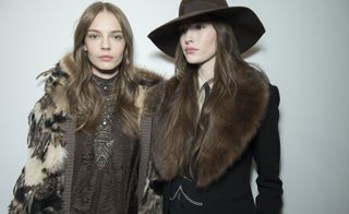 2 models wearing shades of brown winter coats with fur accents and headwear