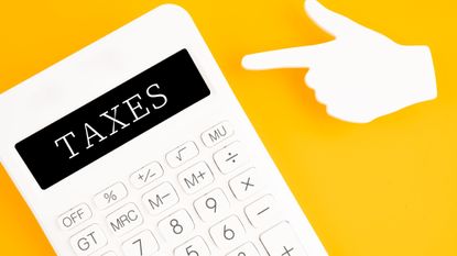 A calculator that says "taxes" with a sticky note finger shape pointing to it on a yellow background.