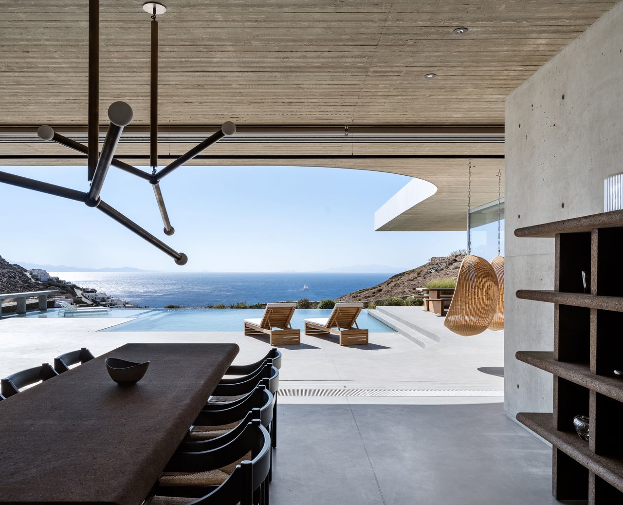 brutalist home by the coast with ocean views, expansive deck with sun loungers by the pool, long dining table, and lots of concrete surfaces