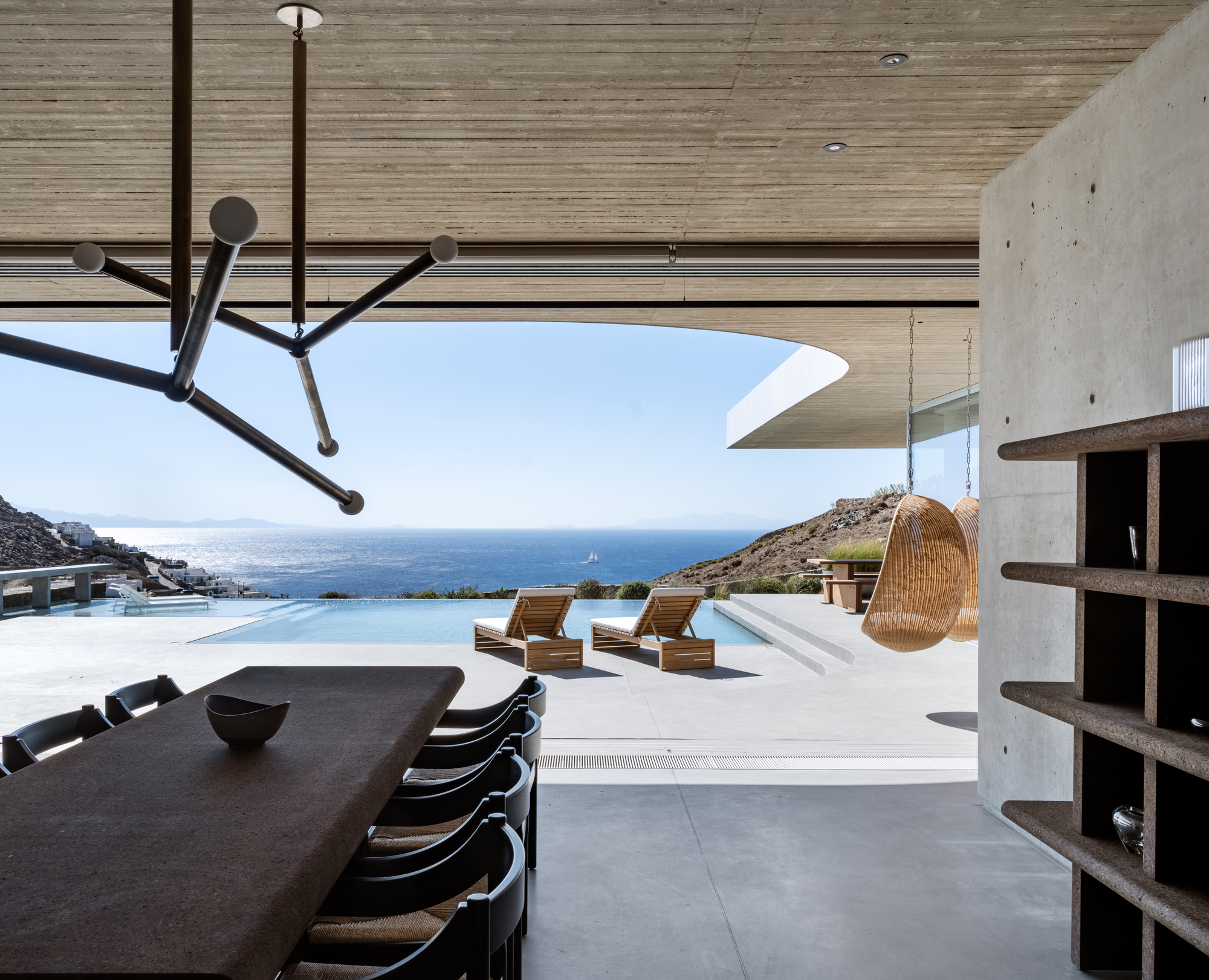 brutalist home by the coast with ocean views, expansive deck with sun loungers by the pool, long dining table, and lots of concrete surfaces
