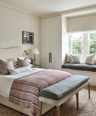 Cream bedroom with cream headboard, pink thrown and bench with gray pillow seat