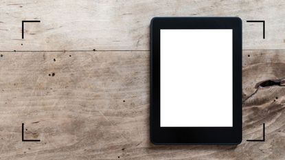 a Kindle with a white screen on a wooden table—to illustrate how to reset a Kindle
