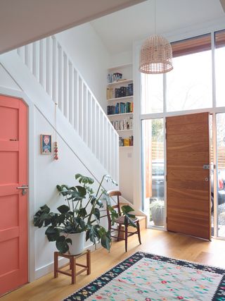 Double height hallway with pink door and wooden flooring