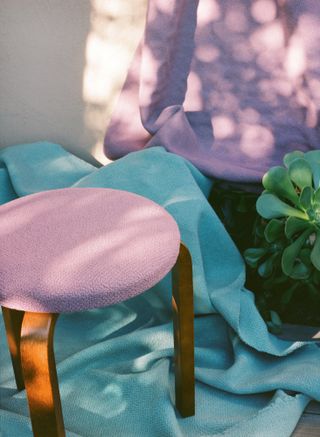 A wooden stool, upholstered in light pink fabric.