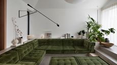 sunken living room with green modular cushions, polished concrete surfaces, indoor plants, ceramic vessels and wall light