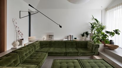 sunken living room with green modular cushions, polished concrete surfaces, indoor plants, ceramic vessels and wall light