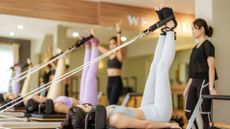 Females in sportswear raising legs and doing hundred exercise on reformer bed during workout in light pilates studio