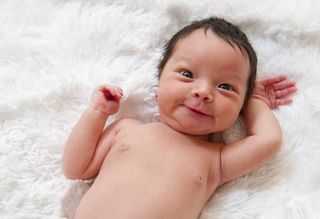 A newborn baby lies smiling on a white blanket.