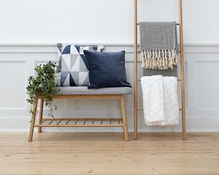 Bench with gray seat pad and blue and blue and gray pillow and ladder with white and patterned blankets draped over it from JYSK
